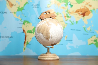 Photo of Wooden toy car on globe against world map. Road trip