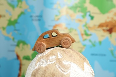 Photo of Wooden toy car on globe against world map, closeup. Road trip