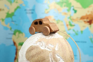 Photo of Wooden toy car on globe against world map, closeup. Road trip