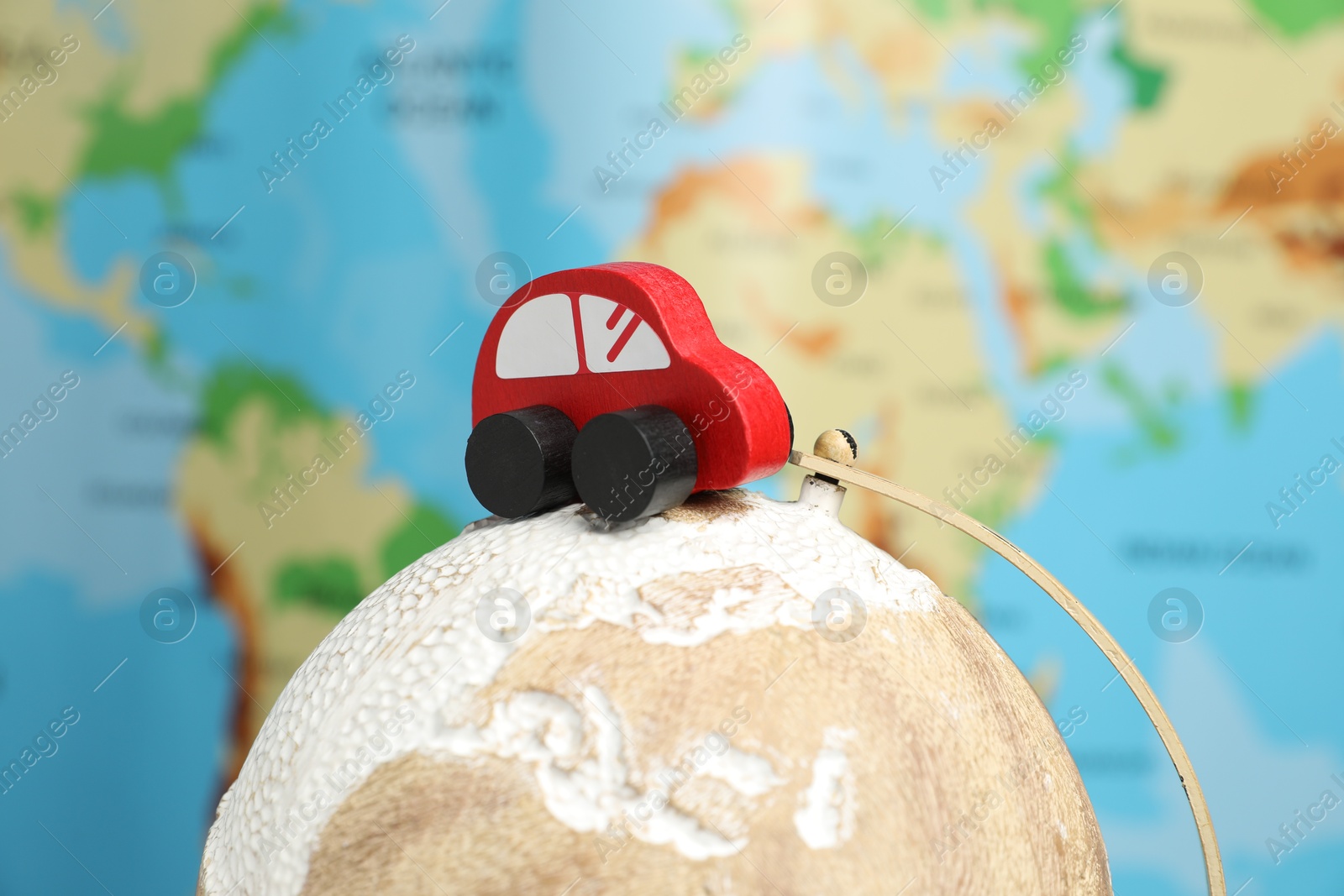 Photo of Red toy car on globe against world map, closeup. Road trip