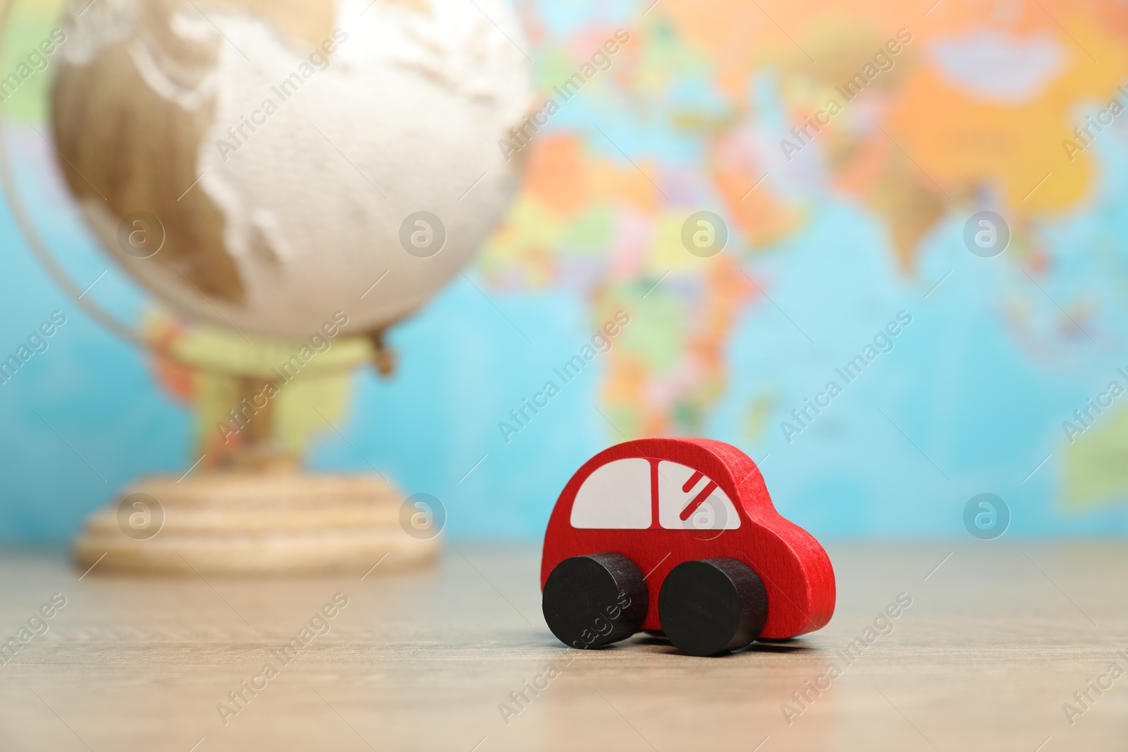 Photo of Red toy car and globe on wooden table against world map, selective focus. Road trip