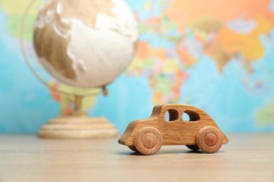 Photo of Wooden toy car and globe on table against world map, selective focus. Road trip