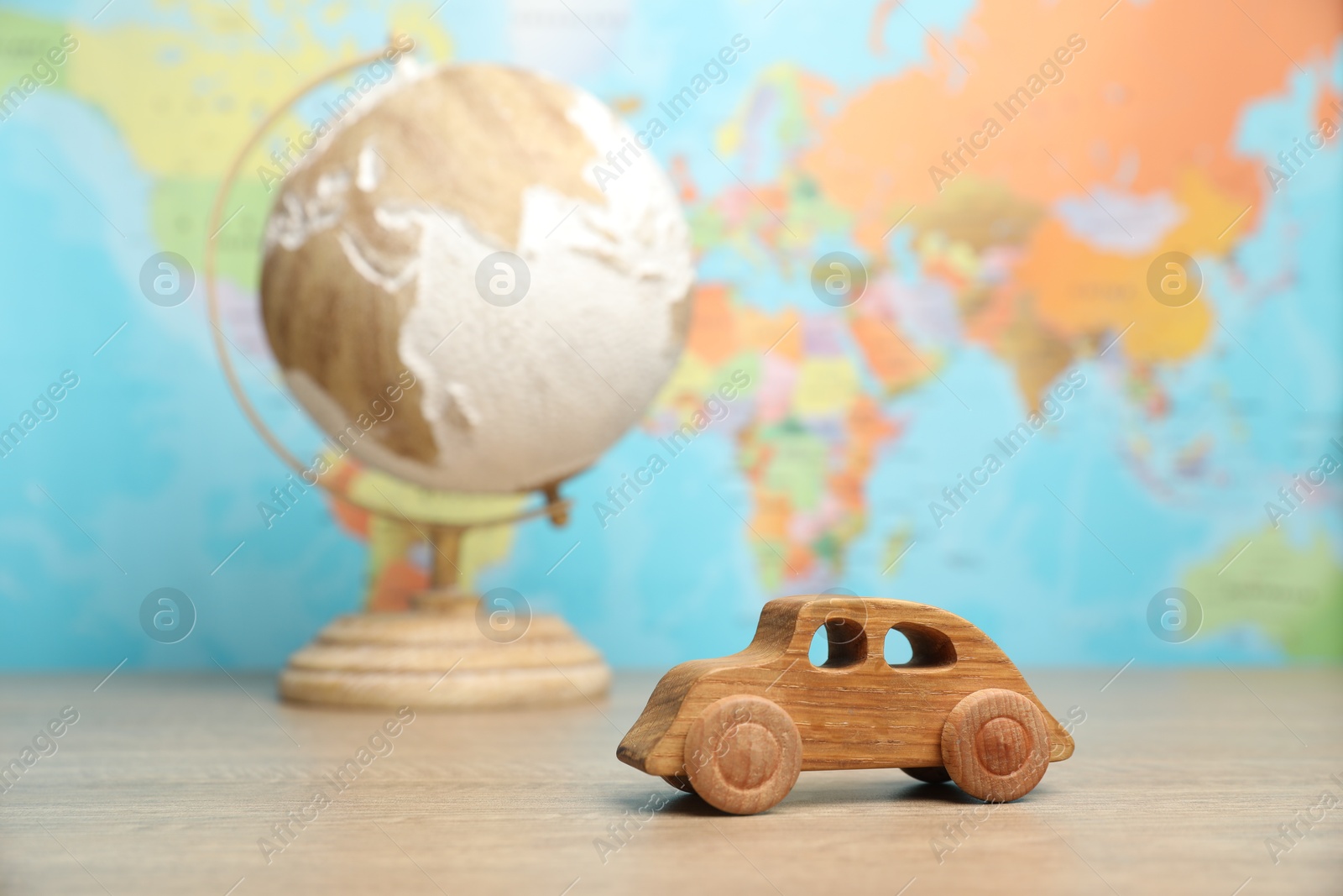 Photo of Wooden toy car and globe on table against world map, selective focus. Road trip