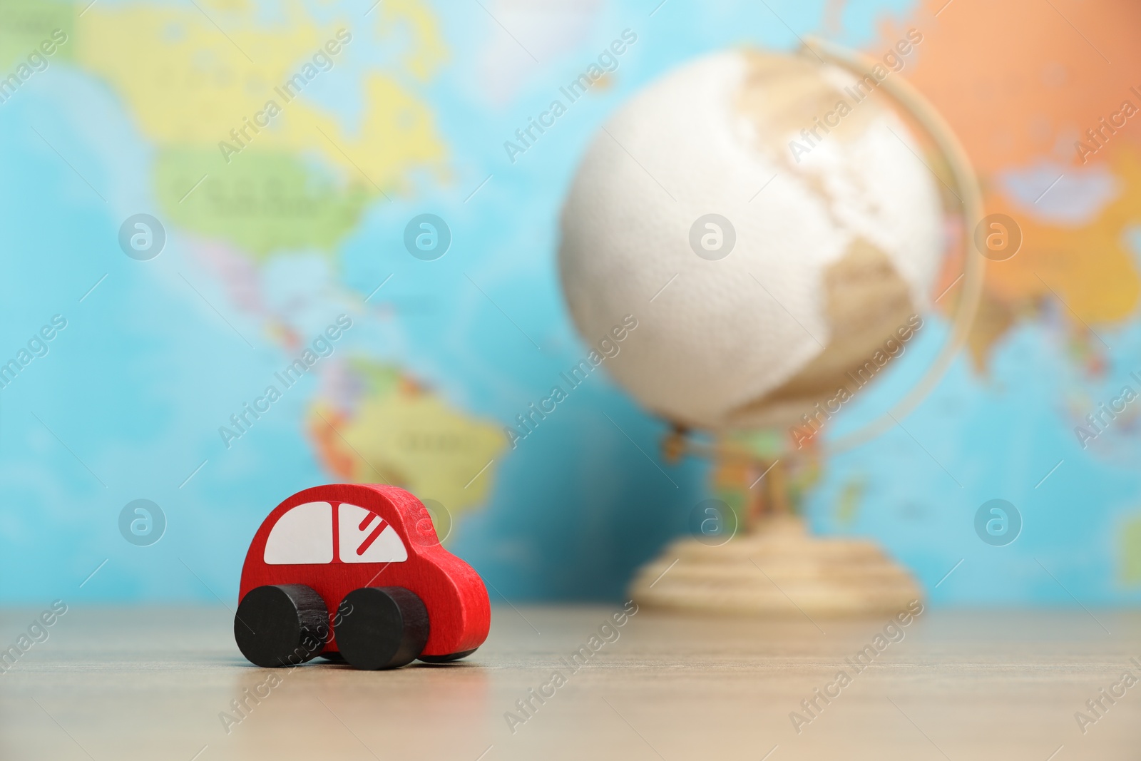 Photo of Red toy car and globe on wooden table against world map, selective focus. Road trip