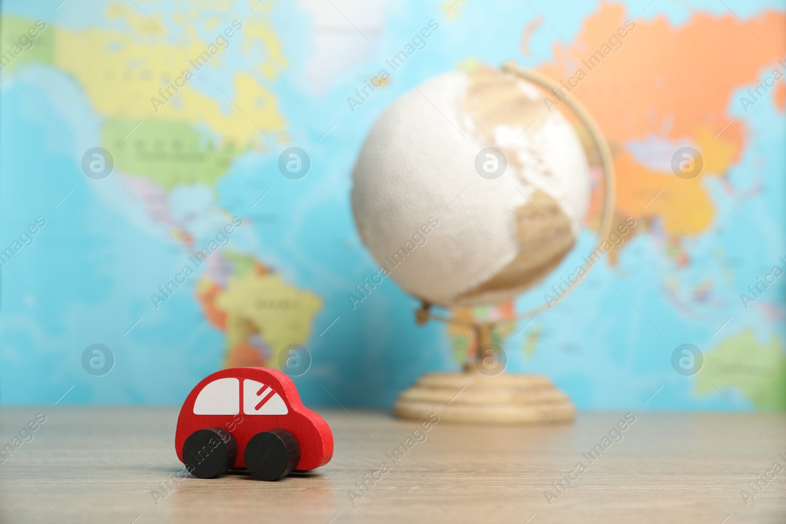 Photo of Red toy car and globe on wooden table against world map, selective focus. Road trip