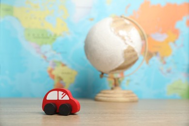 Photo of Red toy car and globe on wooden table against world map, selective focus. Road trip