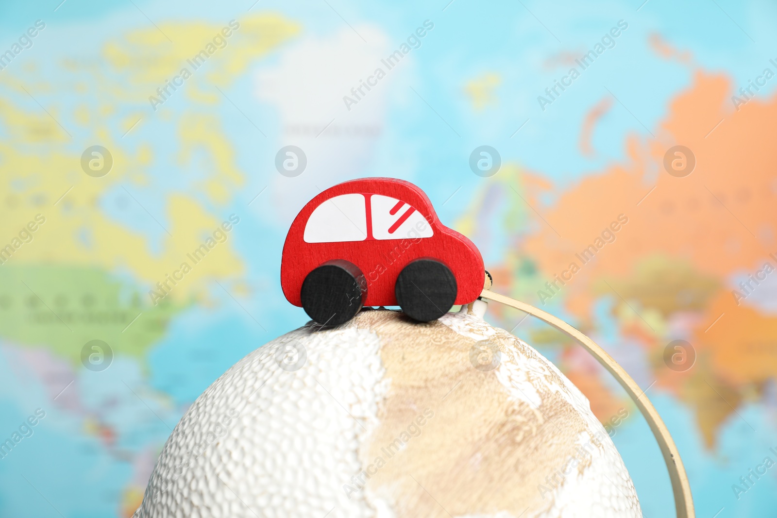 Photo of Red toy car on globe against world map, closeup. Road trip