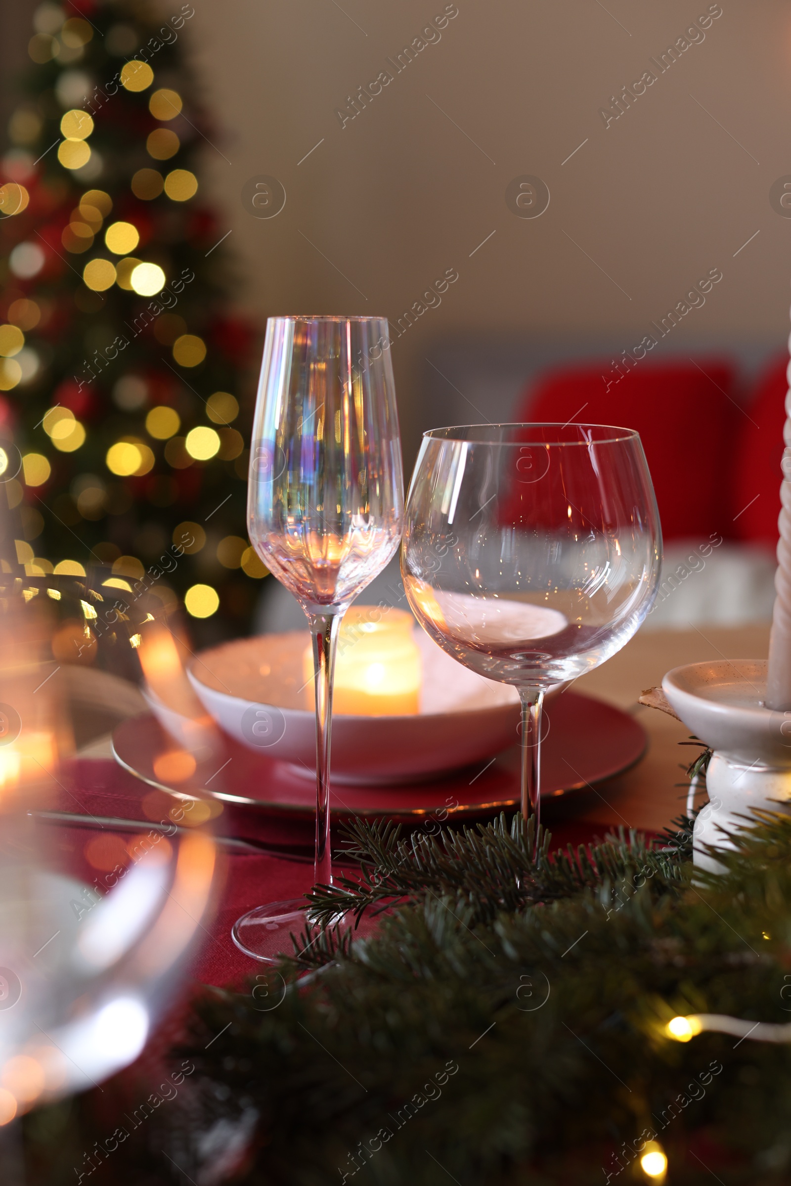 Photo of Beautiful dishware and fir tree branches on table against Christmas lights, closeup