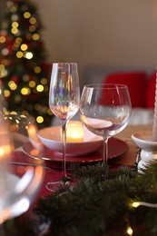 Photo of Beautiful dishware and fir tree branches on table against Christmas lights, closeup