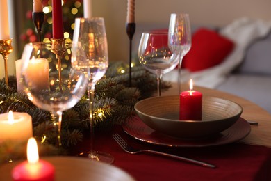 Photo of Beautiful dishware with burning candles, fir tree branches and Christmas lights on wooden table indoors, closeup