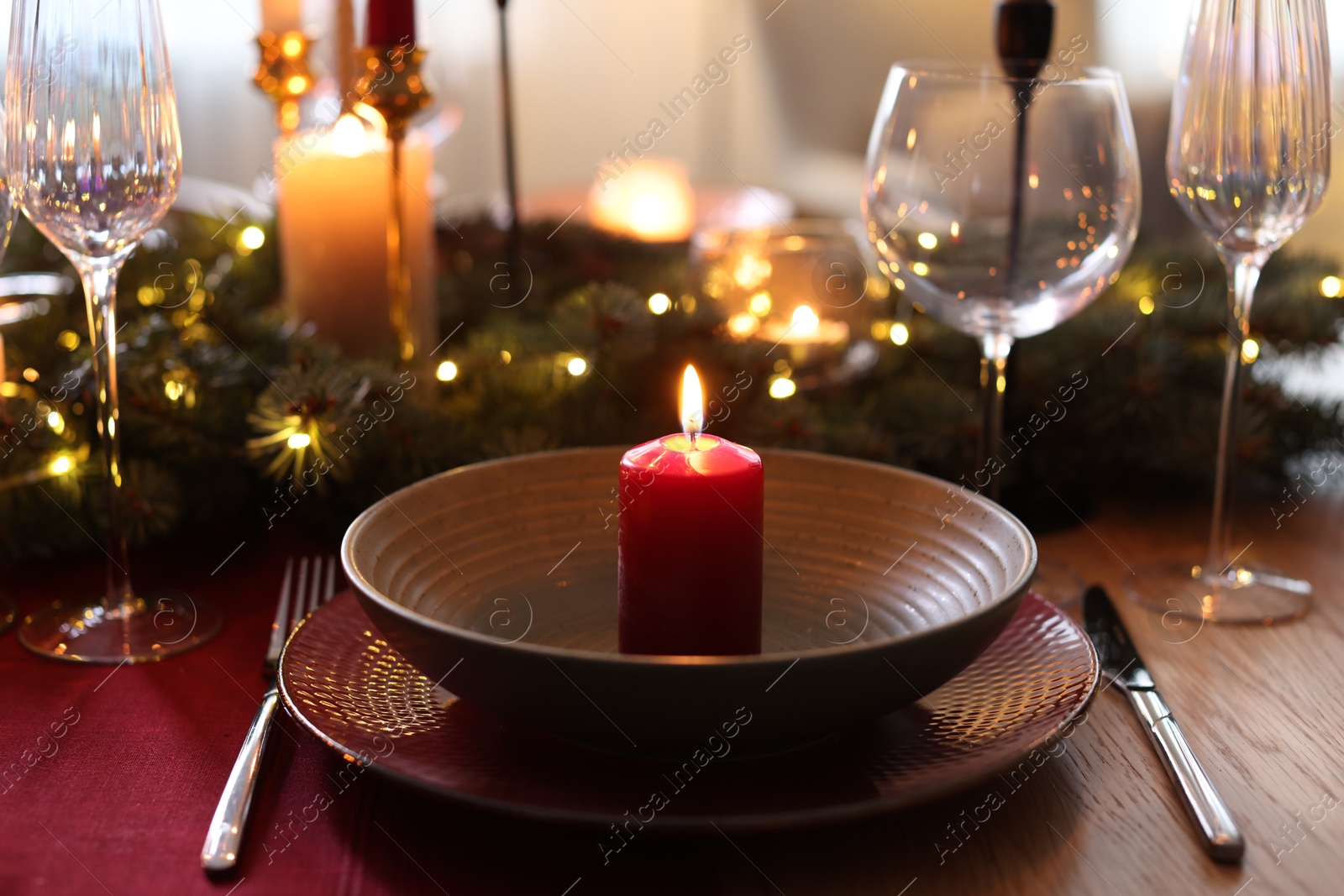 Photo of Beautiful dishware with burning candles, fir tree branches and Christmas lights on wooden table indoors, closeup