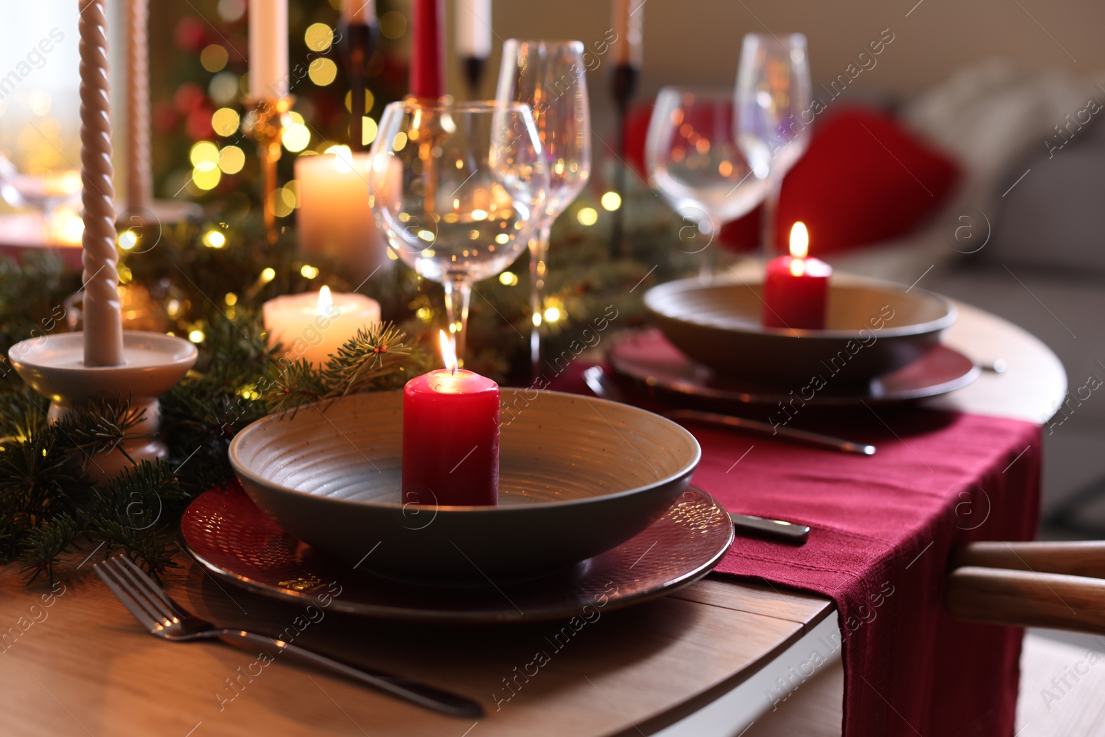 Photo of Beautiful dishware with burning candles, fir tree branches and Christmas lights on wooden table indoors, closeup