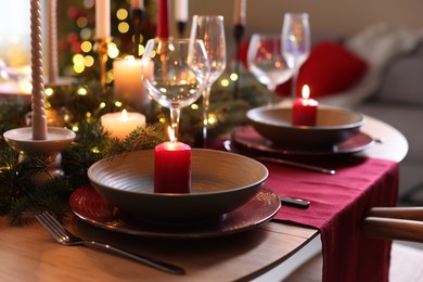 Photo of Beautiful dishware with burning candles, fir tree branches and Christmas lights on wooden table indoors, closeup