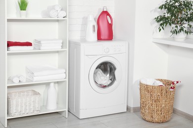 Photo of Washing machine, detergents and basket with laundry in room