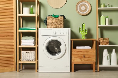 Photo of Washing machine, detergents and basket with laundry in room