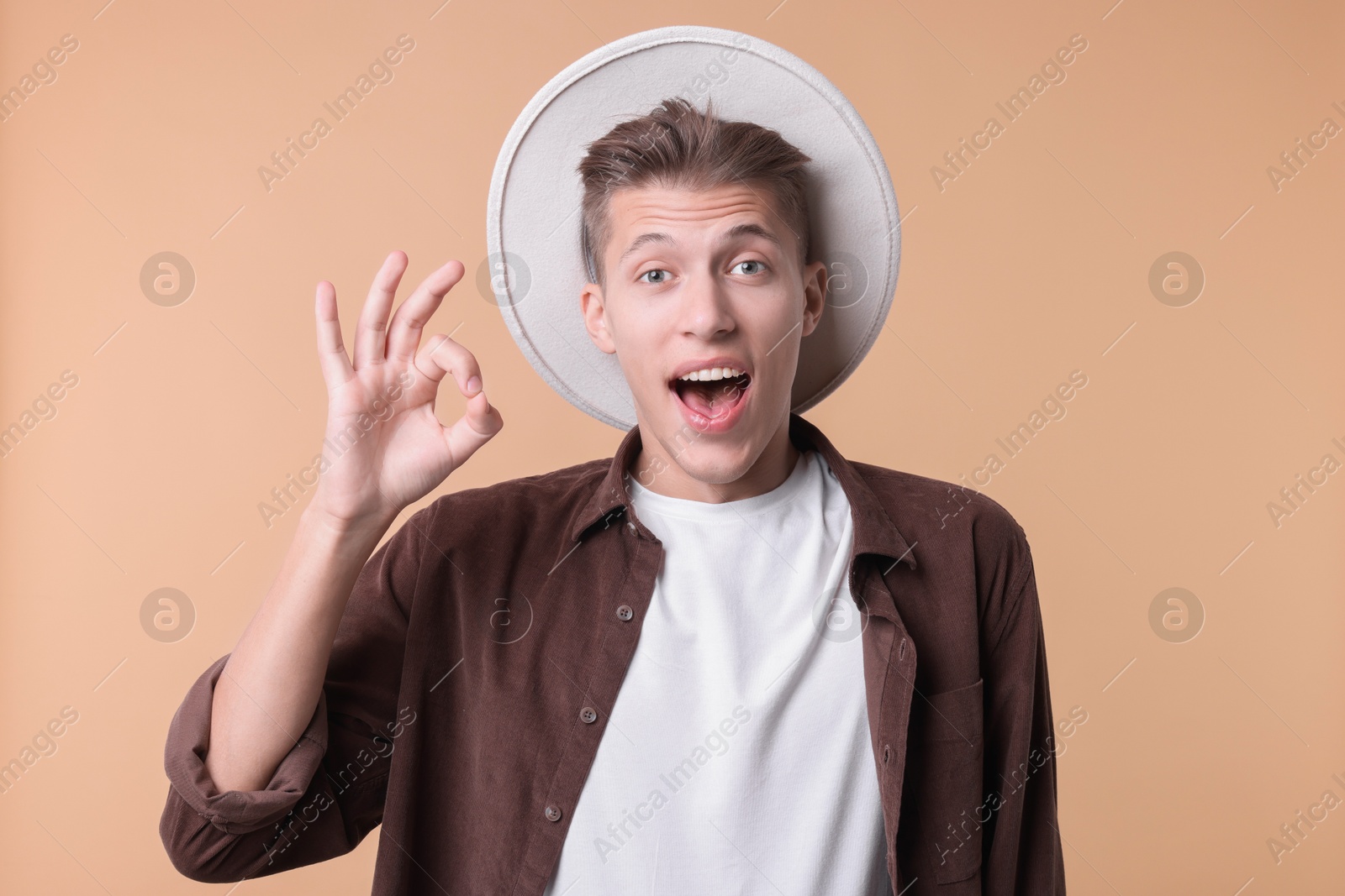 Photo of Emotional young man showing OK gesture on beige background