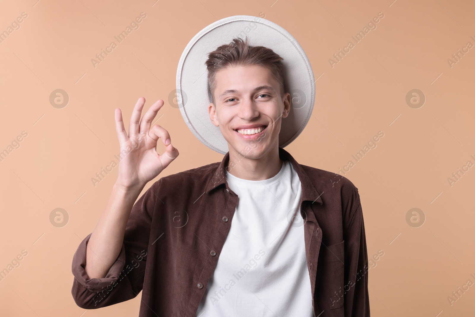 Photo of Happy young man showing OK gesture on beige background