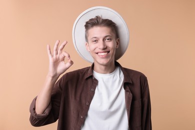 Happy young man showing OK gesture on beige background