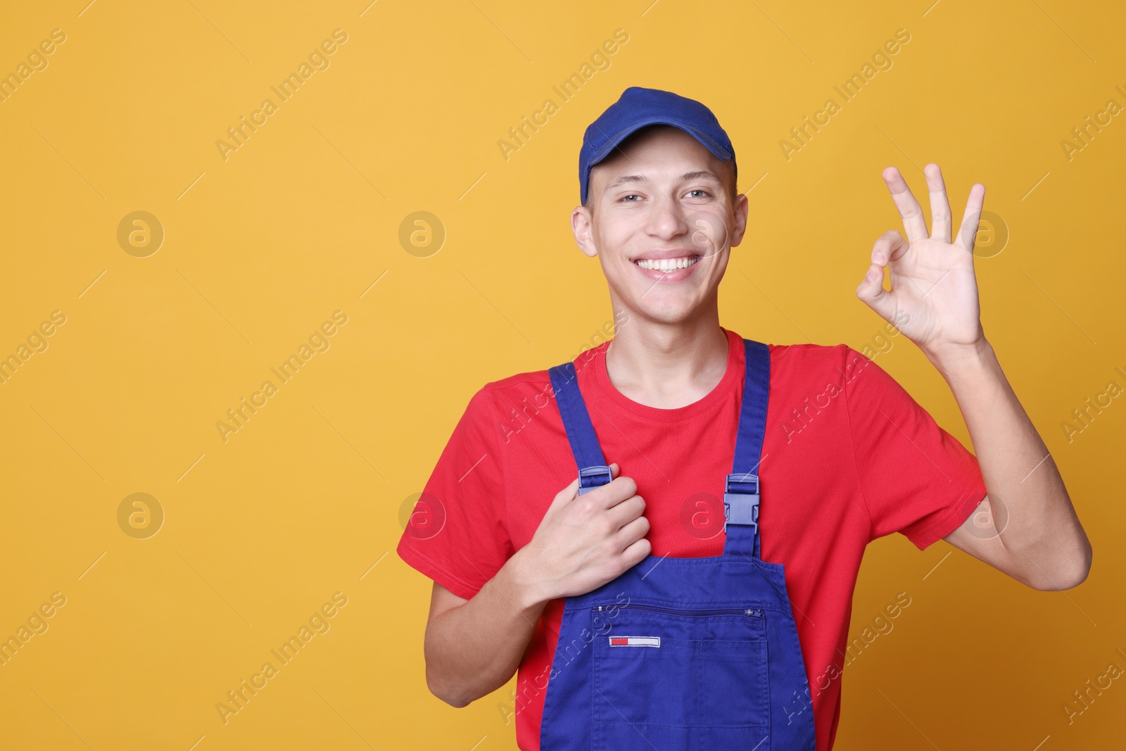 Photo of Happy young man in uniform showing OK gesture on orange background, space for text