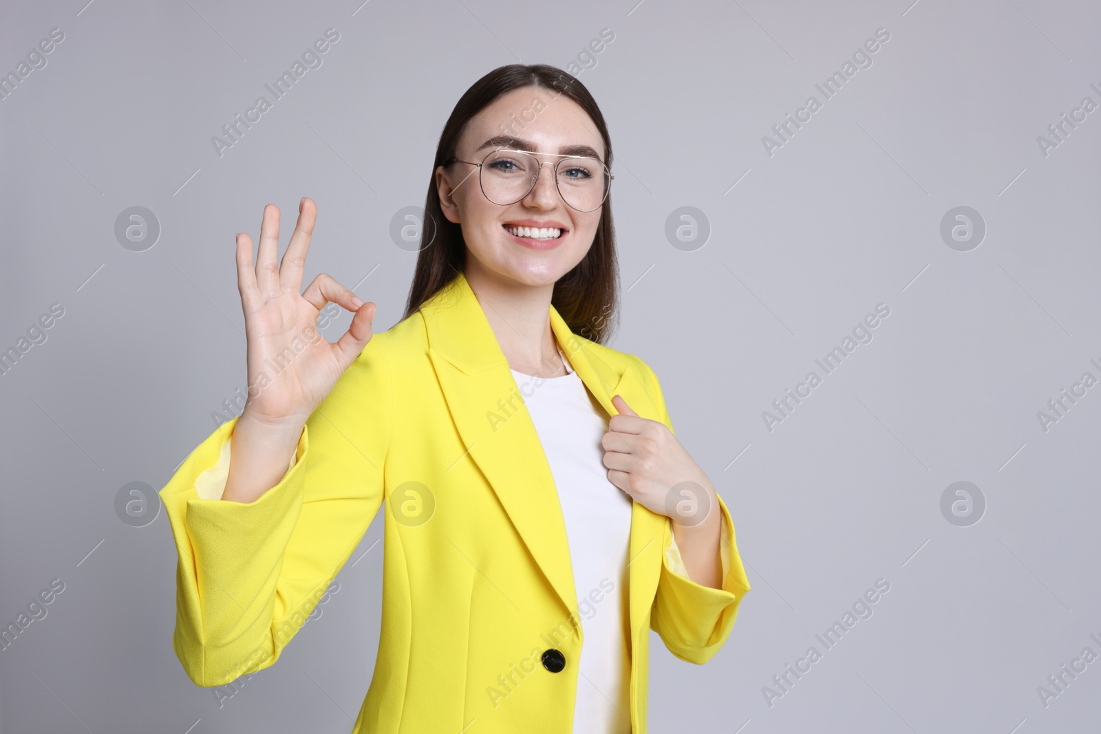 Photo of Happy young woman showing OK gesture on gray background