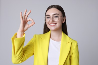 Photo of Happy young woman showing OK gesture on gray background