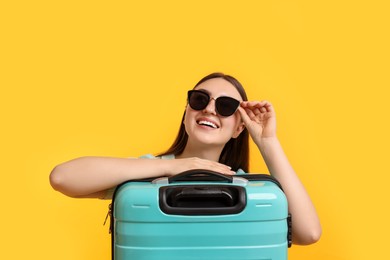 Woman with suitcase wearing sunglasses on orange background