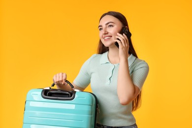 Happy woman with suitcase talking on smartphone against orange background