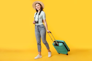 Photo of Happy woman with vintage camera and suitcase on orange background