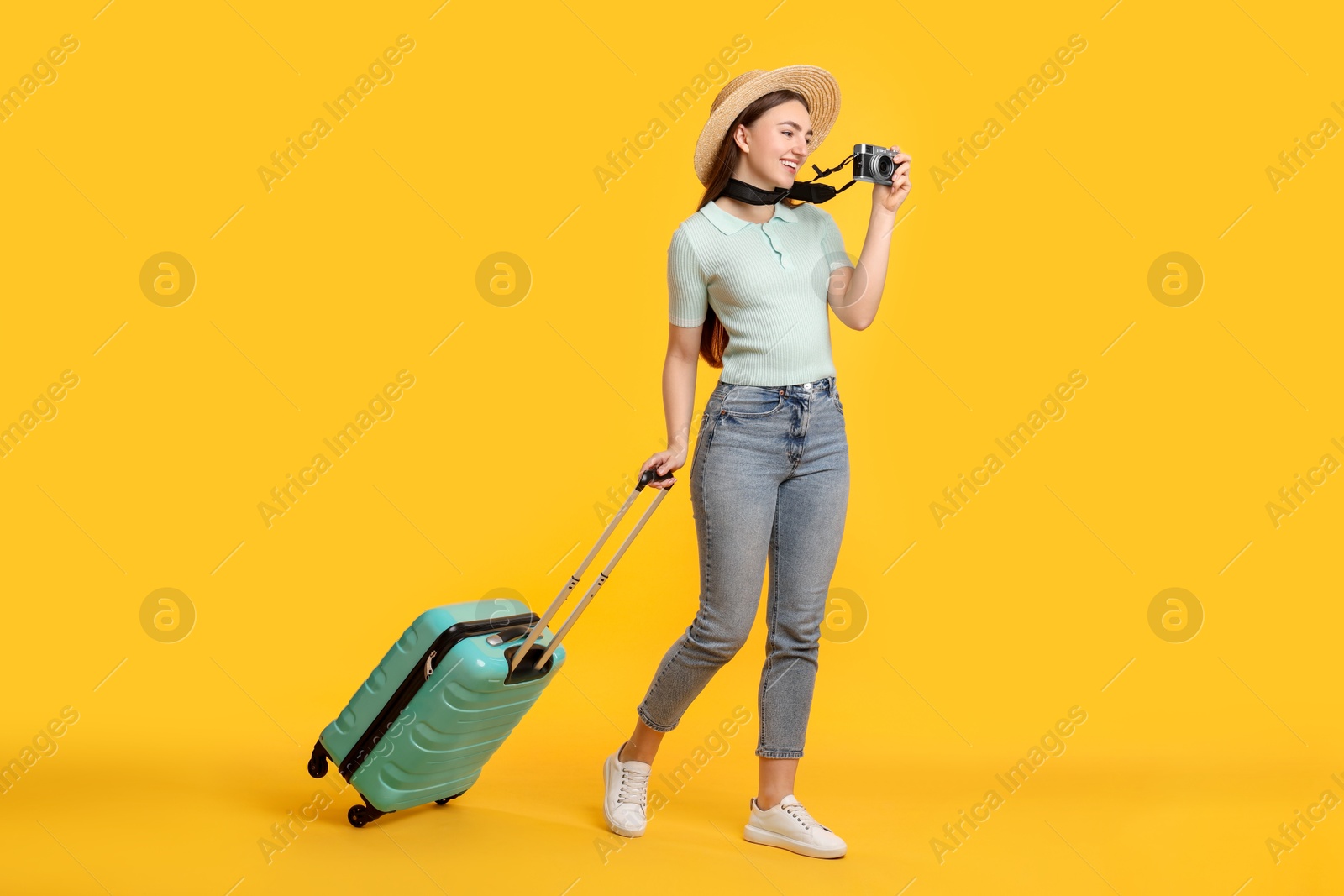 Photo of Happy woman with vintage camera and suitcase on orange background