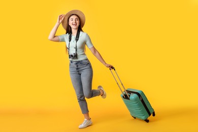 Photo of Happy woman with vintage camera and suitcase on orange background