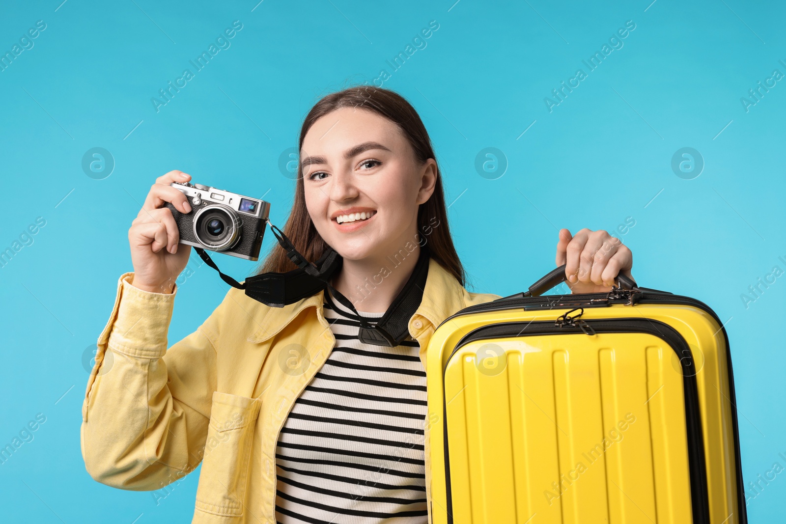 Photo of Woman with vintage camera and suitcase on light blue background