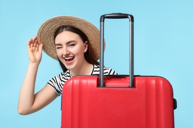 Woman in straw hat with suitcase on light blue background