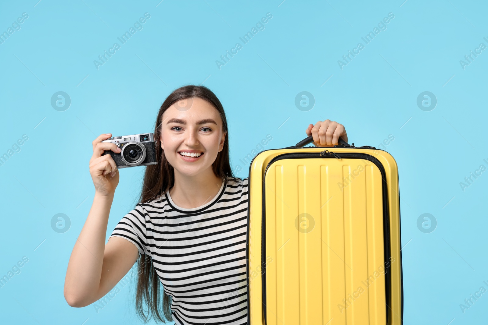 Photo of Woman with vintage camera and suitcase on light blue background