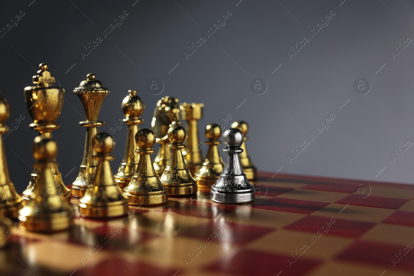 Photo of Silver pawn in front of golden chess pieces on chessboard against grey background, closeup and space for text. Competition concept