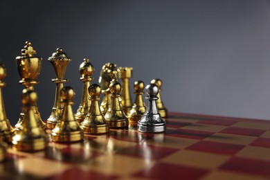 Photo of Silver pawn in front of golden chess pieces on chessboard against grey background, closeup and space for text. Competition concept