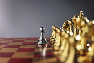 Photo of Silver pawn in front of golden chess pieces on chessboard against grey background, closeup and space for text. Competition concept