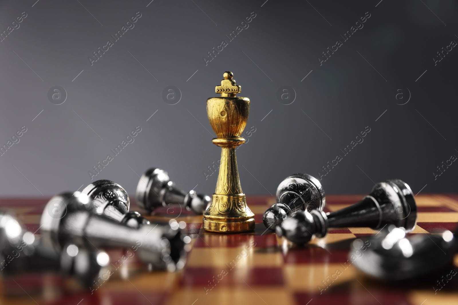 Photo of Golden chess king among fallen silver pieces on chessboard against grey background, closeup. Competition concept