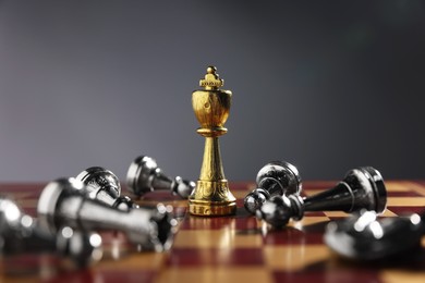 Photo of Golden chess king among fallen silver pieces on chessboard against grey background, closeup. Competition concept