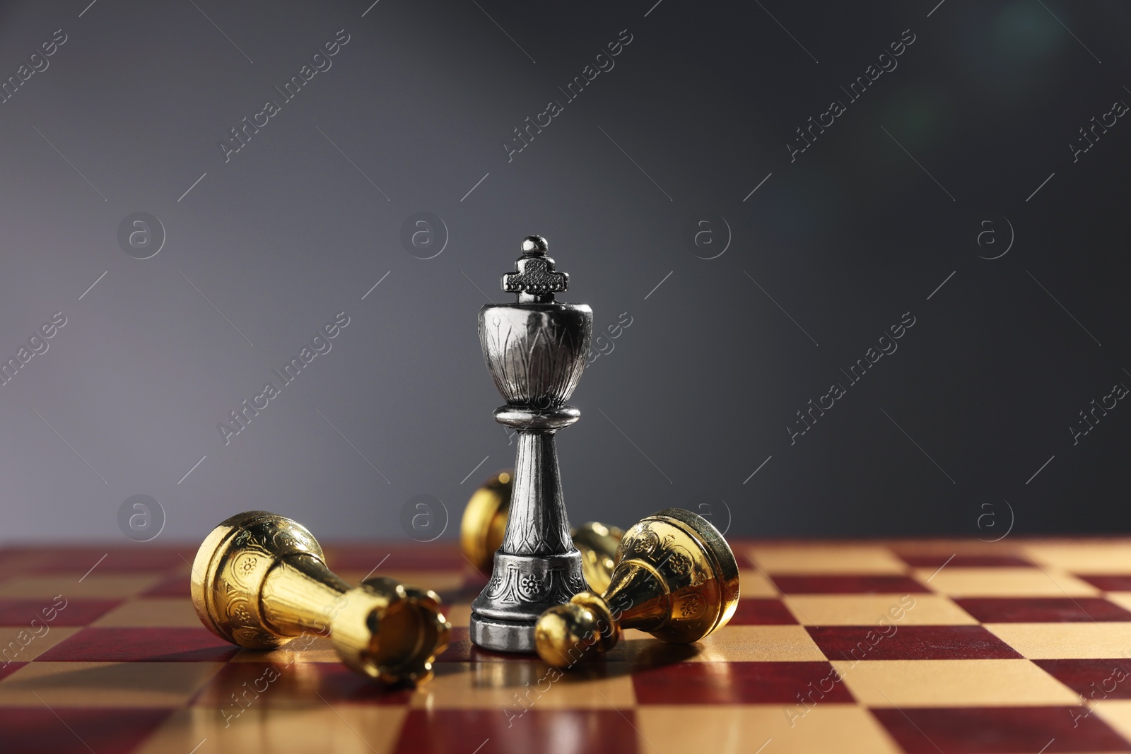 Photo of Silver chess king among fallen golden pieces on chessboard against grey background, closeup. Competition concept