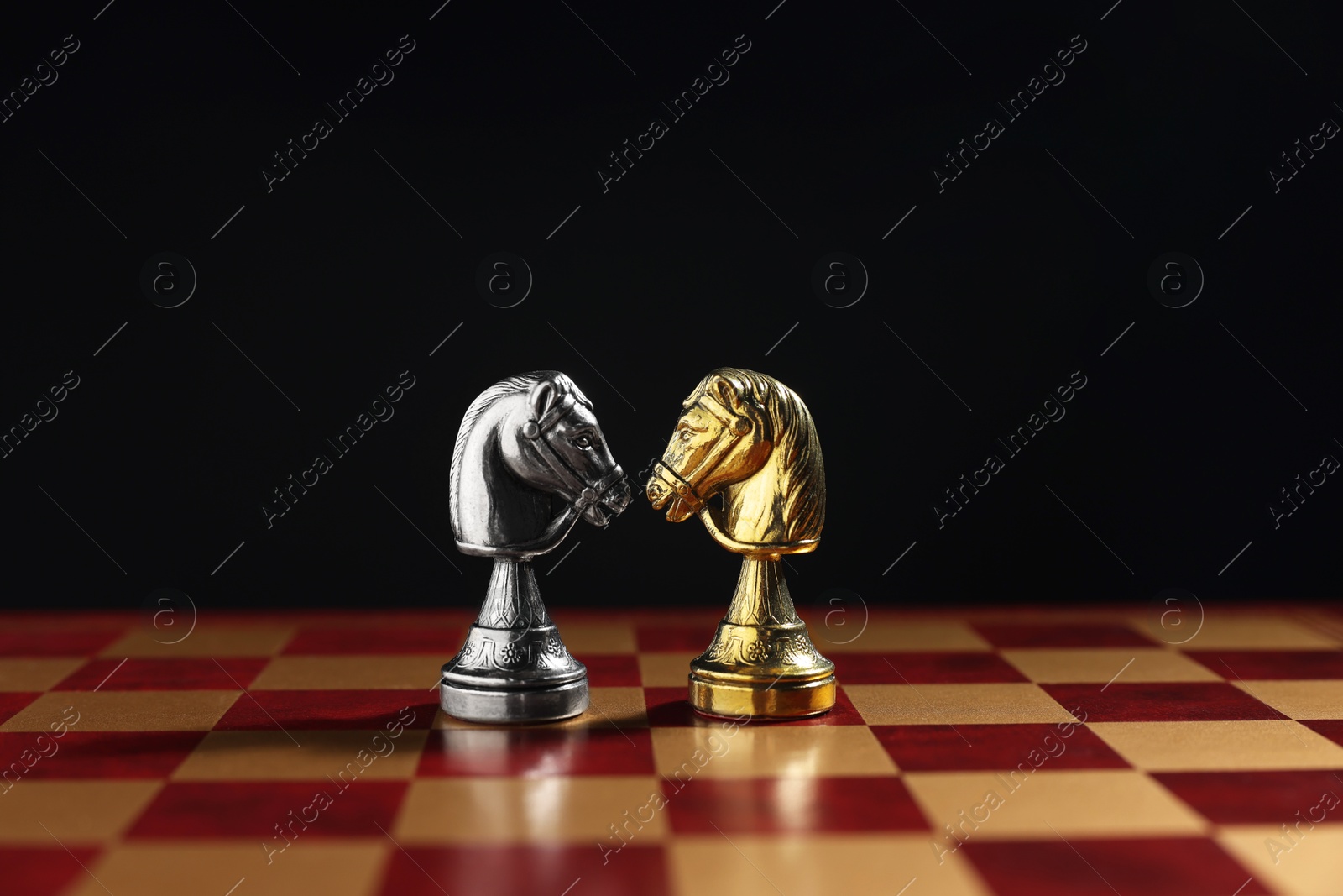 Photo of Golden and silver knights on chessboard against black background, closeup. Competition concept