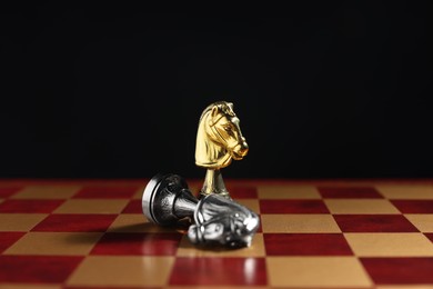 Photo of Golden knight and fallen silver one on chessboard against black background, closeup. Competition concept