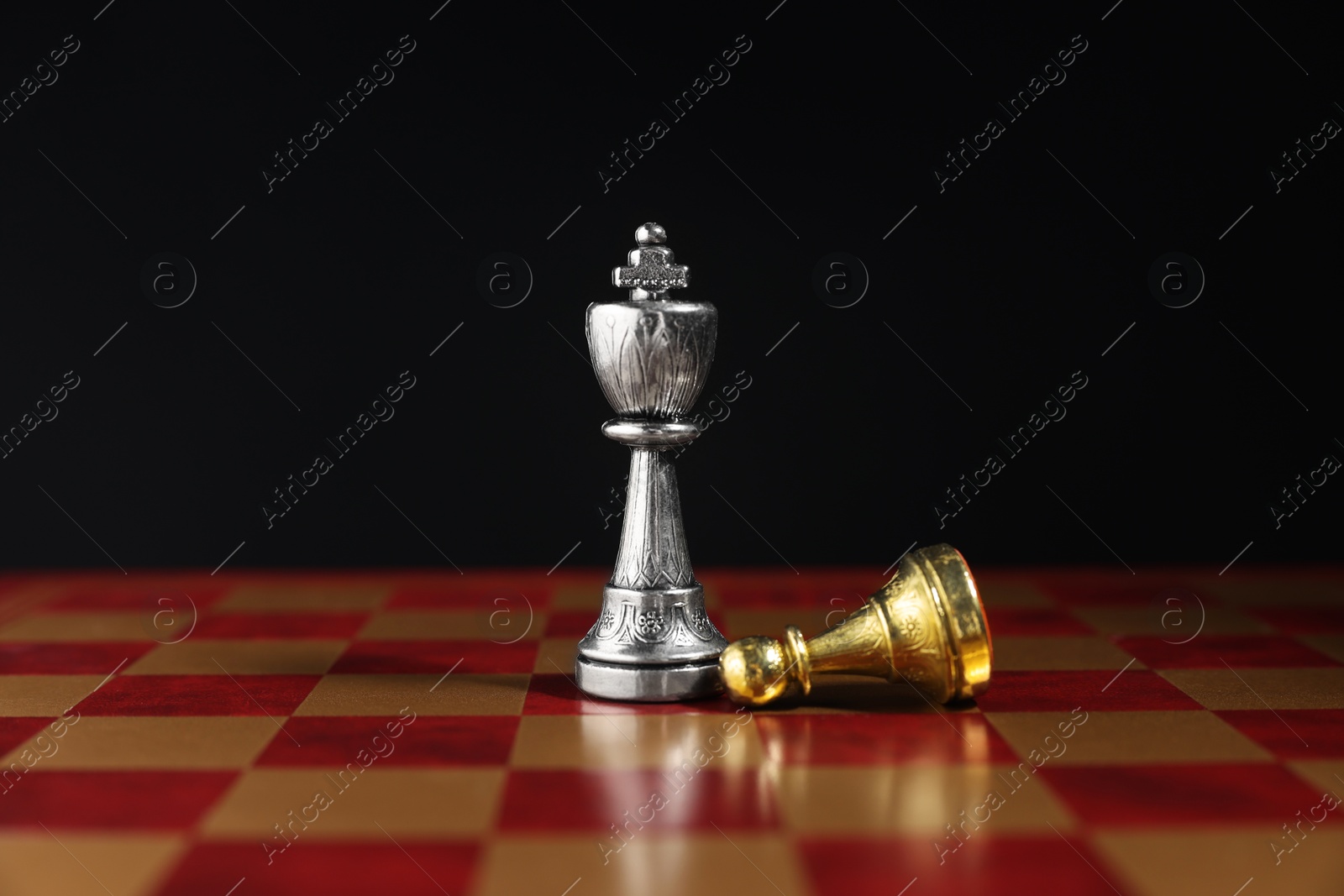 Photo of Silver king and fallen golden pawn on chessboard against black background, closeup. Competition concept