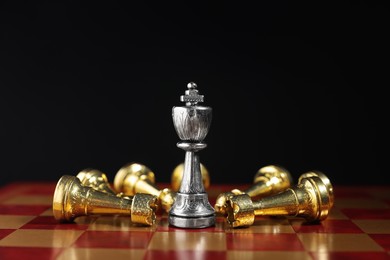 Photo of Silver chess king among fallen golden pieces on chessboard against black background, closeup. Competition concept