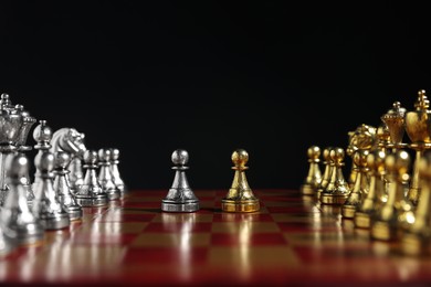 Photo of Golden and silver pawns near other chess pieces on chessboard against black background, closeup. Competition concept