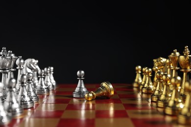 Photo of Silver pawn near fallen golden one and other chess pieces on chessboard against black background, closeup. Competition concept