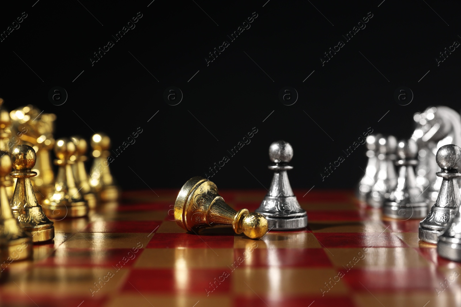 Photo of Silver pawn near fallen golden one and other chess pieces on chessboard against black background, closeup. Competition concept