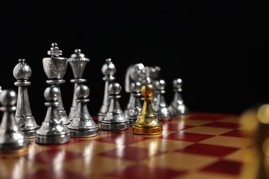 Photo of Golden pawn in front of silver chess pieces on chessboard against black background, closeup. Competition concept