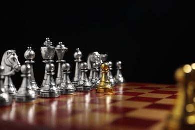 Photo of Golden pawn in front of silver chess pieces on chessboard against black background, closeup. Competition concept