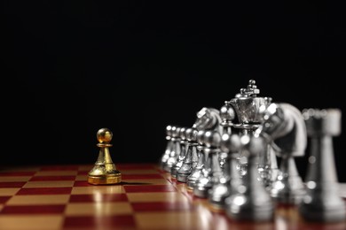 Photo of Golden pawn in front of silver chess pieces on chessboard against black background, closeup. Competition concept