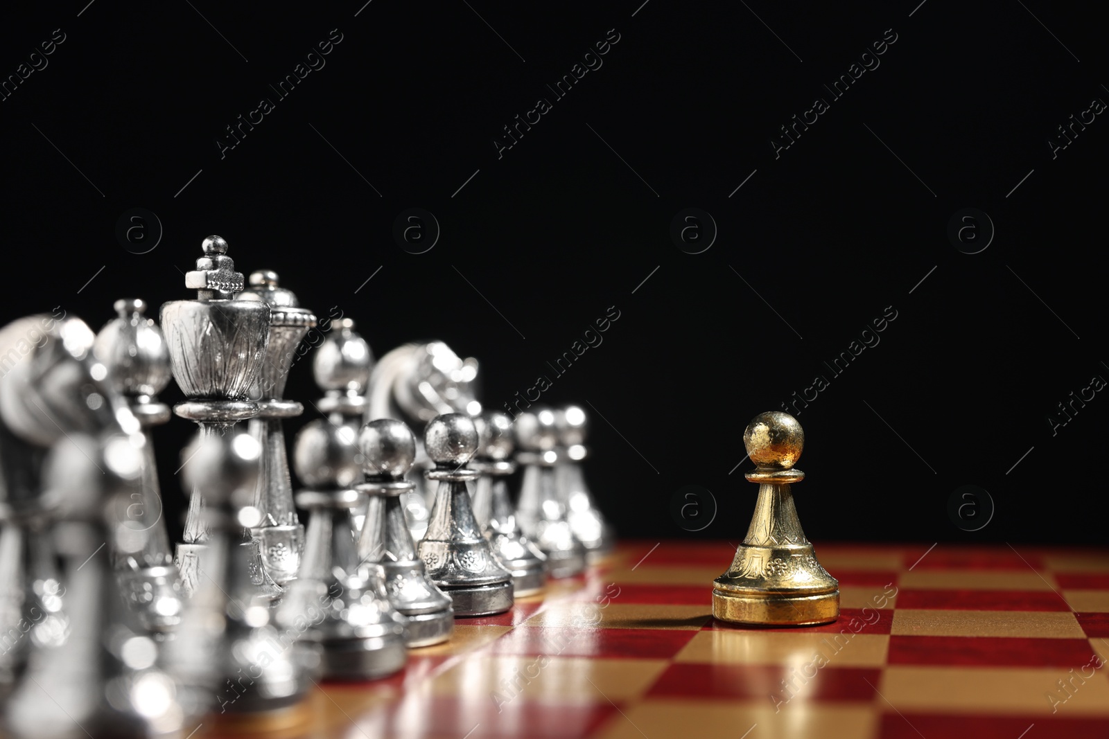 Photo of Golden pawn in front of silver chess pieces on chessboard against black background, closeup. Competition concept